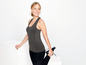 Eine Frau in einem grauen Tanktop und schwarzen Leggings streckt ihr Bein.