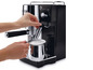 Eine schwarze De'Longhi Espressomaschine mit Milchaufschäumer in Gebrauch.