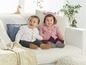 Zwei Babys in Strickjacken sitzen auf einer Couch.
