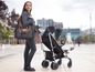 Eine Frau mit einer Oh My Baby Wickeltasche schiebt einen schwarzen Kinderwagen auf der Straße.