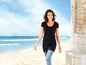 Frau in einer schwarzen Tunika und blauen Jeans am Strand.