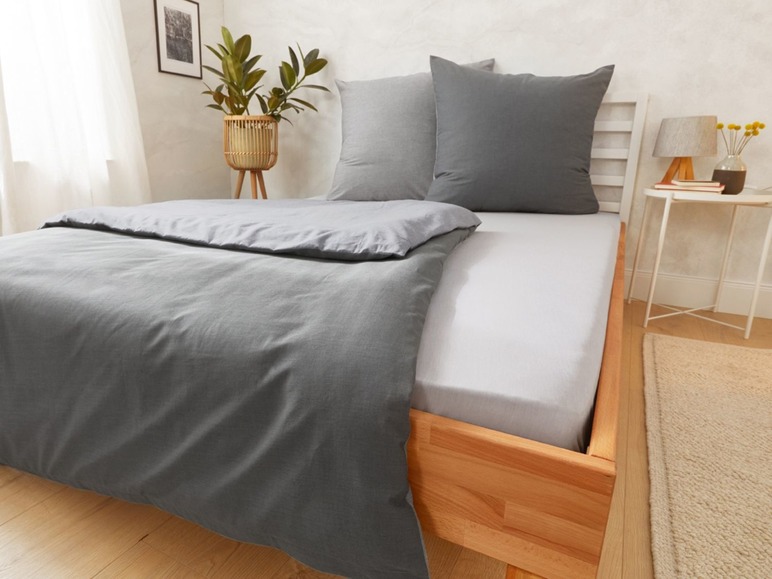 Ein graues Bettlaken und Kissen auf einem Holzbettgestell.