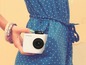Eine Frau in einem blauen Kleid mit weißen Punkten hält eine Polaroid-Kamera.