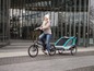 Eine Frau fährt ein schwarzes Mate E-Bike mit einem Qeridoo Kinderwagen.
