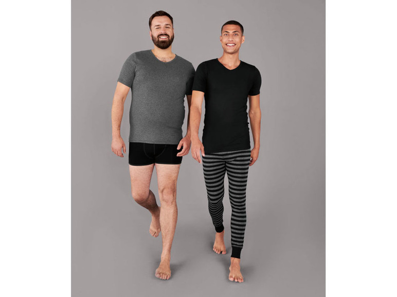 Zwei Männer in Unterwäsche, einer mit einem grauen T-Shirt und einer mit einem schwarzen T-Shirt und gestreiften Schlafanzughose.