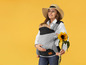 Eine Frau trägt ein Baby in einer Tragehilfe und hält eine Sonnenblume.