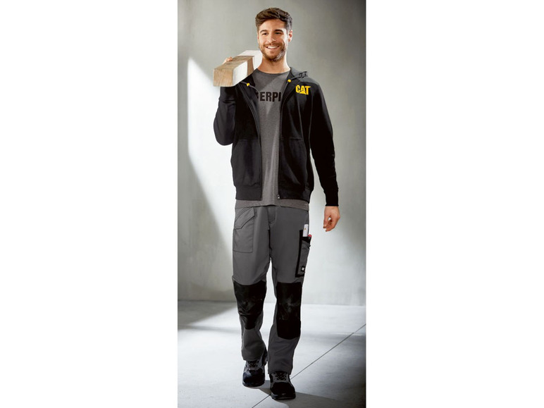 Mann trägt eine schwarze Caterpillar-Kapuzenjacke und graue Arbeitshose.