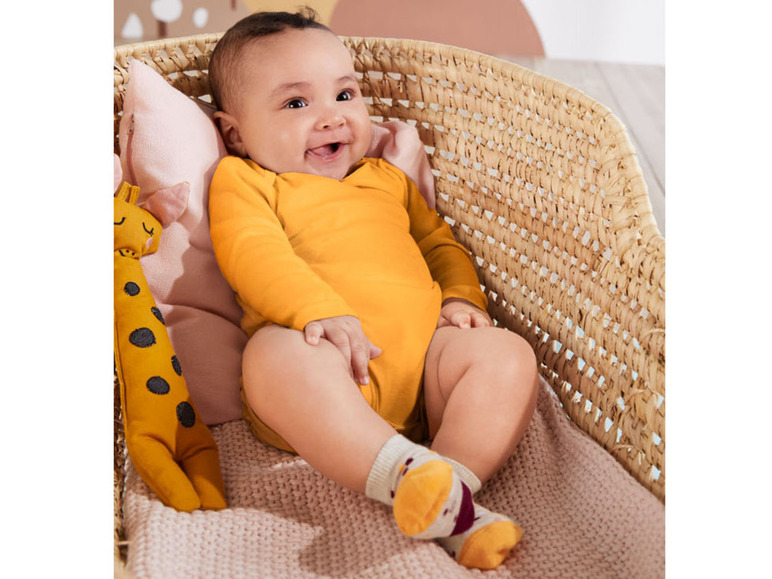 Ein Baby in einem gelben Strampler mit Socken und einem Giraffen-Plüschtier.