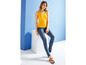 Eine Frau trägt ein gelbes Tanktop und blaue Skinny Jeans.