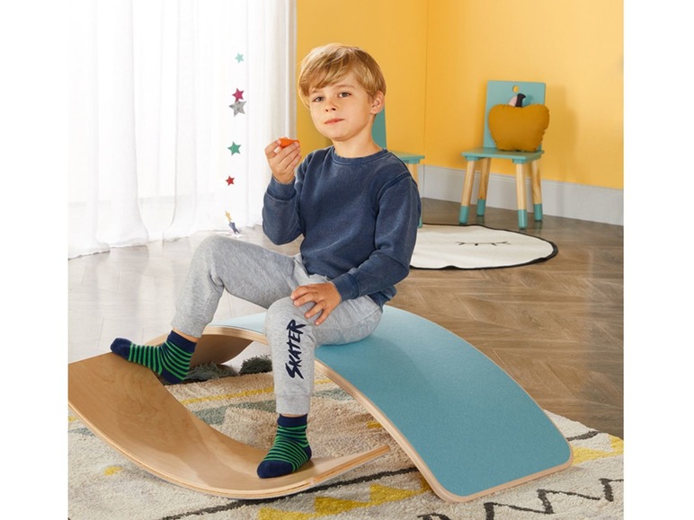 Ein Kind sitzt auf einem Holz-Balanceboard mit blauer Polsterung.