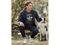 Mann mit Hoodie und Jeans posiert mit einem Hund.