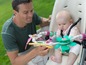 Ein Vater hält ein Baby in einem Hochstuhl mit einem Fisher-Price Spielzeug.