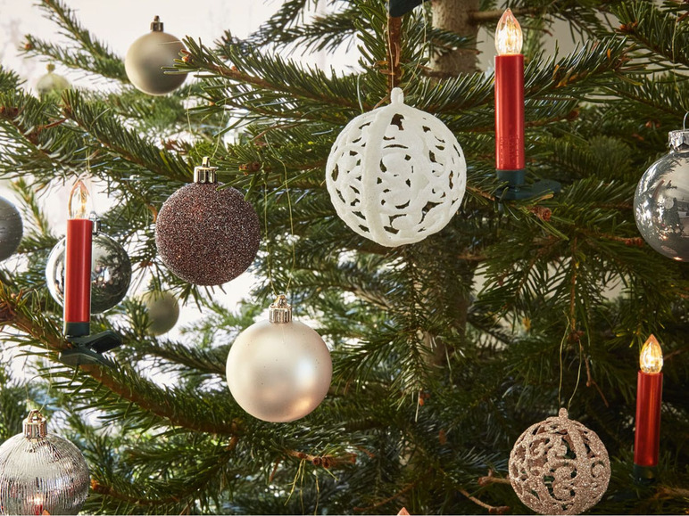 Weihnachtsbaum mit silbernen, goldenen und weißen Kugeln und roten Kerzen geschmückt.