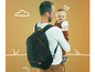 Ein Mann trägt ein Baby und einen schwarzen Babymoov-Rucksack mit weißen Punkten.