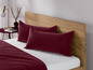 Bordeauxfarbene Bettwäsche mit zwei Kissenbezügen auf einem Holzbett.