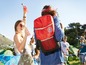 Eine Person trägt einen roten 'Cool Bag' Rucksack auf einem Festival.