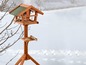 Ein Holzvogelhaus mit zwei Futterbehältern im Schnee.