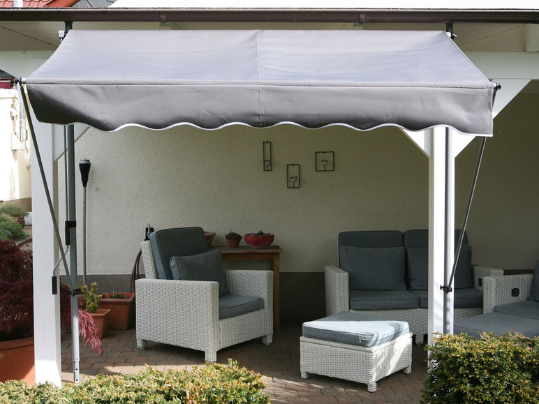 Eine weiße Terrasse mit einem grauen Sonnensegel, Rattansesseln und einem Hocker.