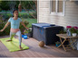 Eine Frau macht Yoga auf einer Holzterrasse mit einer Aufbewahrungsbox daneben.
