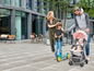 Eine Familie mit einem Baby im Kinderwagen, einem Kind auf einem Roller und Stühlen im Freien.