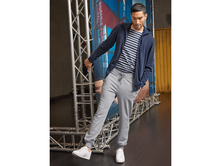 Mann in dunkelblauer Kapuzenjacke, grauen Jogginghose und weißen Sneakern.