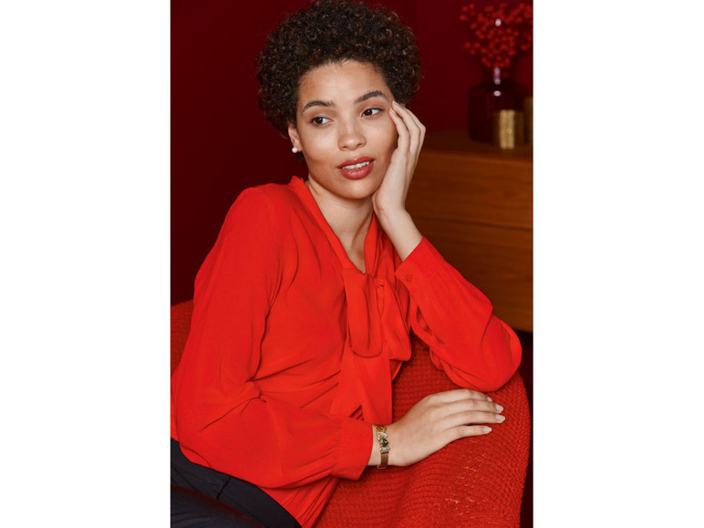 Eine Frau in einem roten Oberteil mit einer goldenen Herz-Armbanduhr.