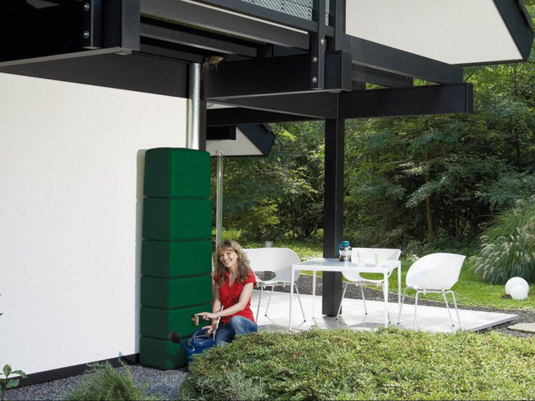 Ein grüner Regenton neben einer Terrasse mit weißen Stühlen.