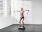 Eine Frau trainiert auf einer Vibrations-Plattform mit Widerstandsbändern.