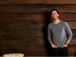 Mann in einem grauen T-Shirt vor einem Holzhintergrund.