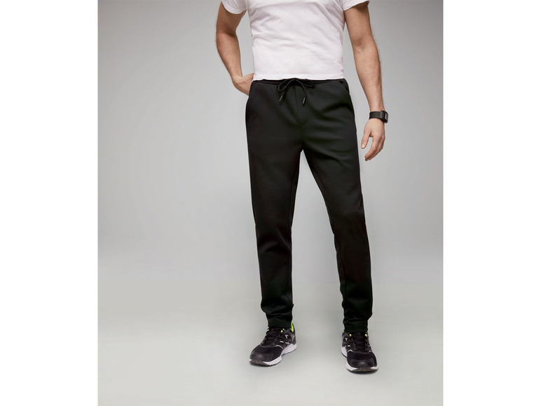 Mann trägt schwarze Jogginghose und ein weißes T-Shirt.