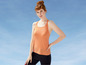 Eine Frau in einem orangefarbenen Sporttop und schwarzen Leggings vor blauem Himmel.