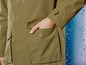 Eine grüne Regenjacke mit Taschen und einer Hand in der Tasche.
