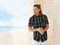 Mann trägt ein kariertes Hemd und weiße Hose am Strand.