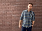 Mann in einem karierten Hemd vor einer Ziegelwand.