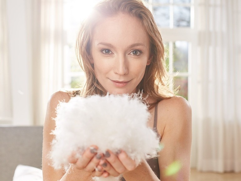 Eine Frau hält ein flauschiges Kissen voller Daunen.