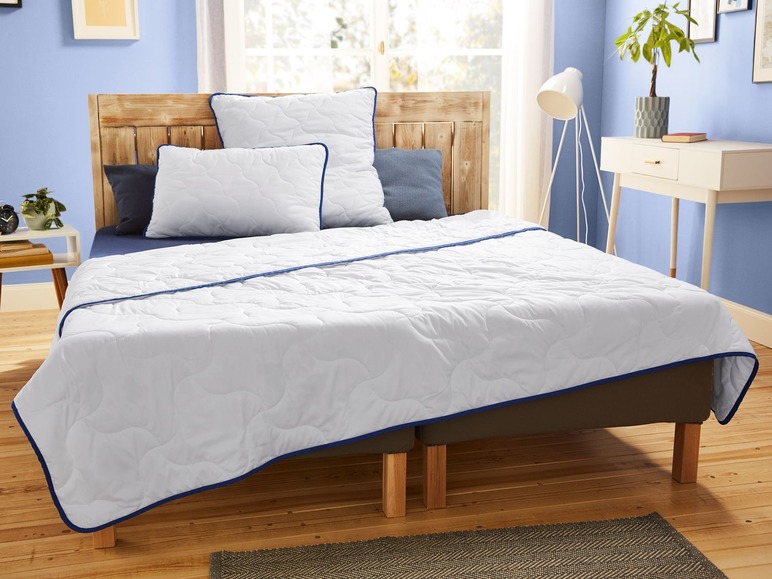 Ein weißes Bettdecken-Set mit blauen Paspeln auf einem Bett mit Kissen.