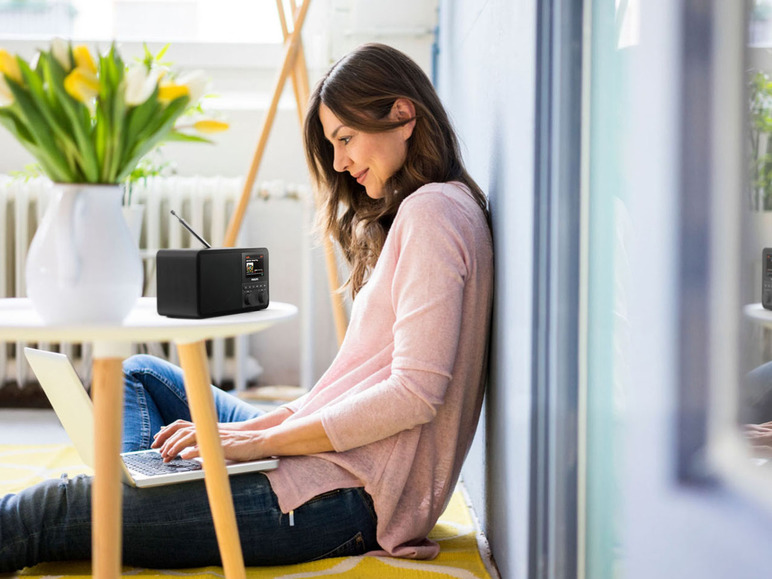 Eine Frau arbeitet an ihrem Laptop mit einem tragbaren Radio und Blumen im Hintergrund.