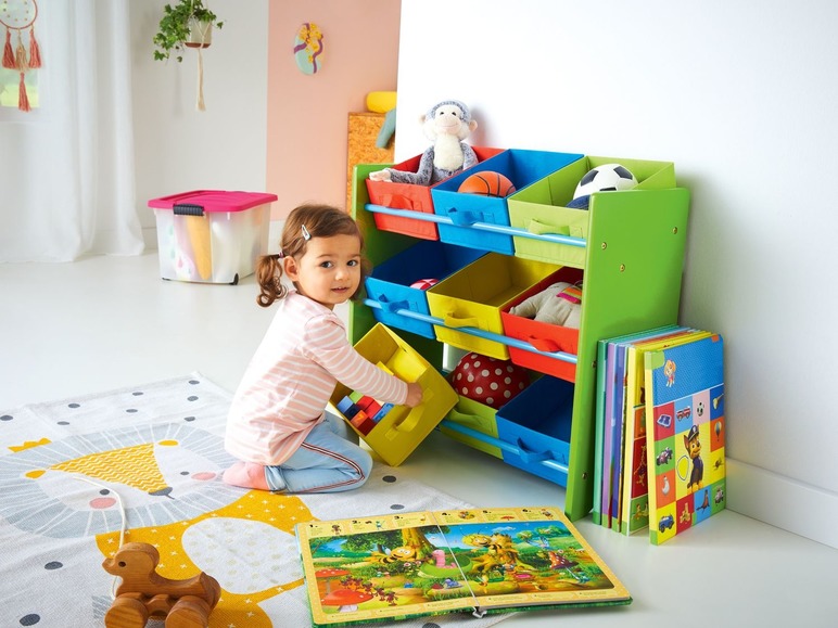 Ein Kind spielt mit Spielzeug in einem farbenfrohen Aufbewahrungsschrank mit Büchern und einer Spielmatte.