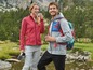 Ein Mann und eine Frau in Fleecejacken trinken aus Thermosbechern bei einer Wanderung in der Natur.