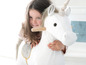 Ein Mädchen in einem rosa Pullover reitet auf einem weißen Plüsch-Einhorn.