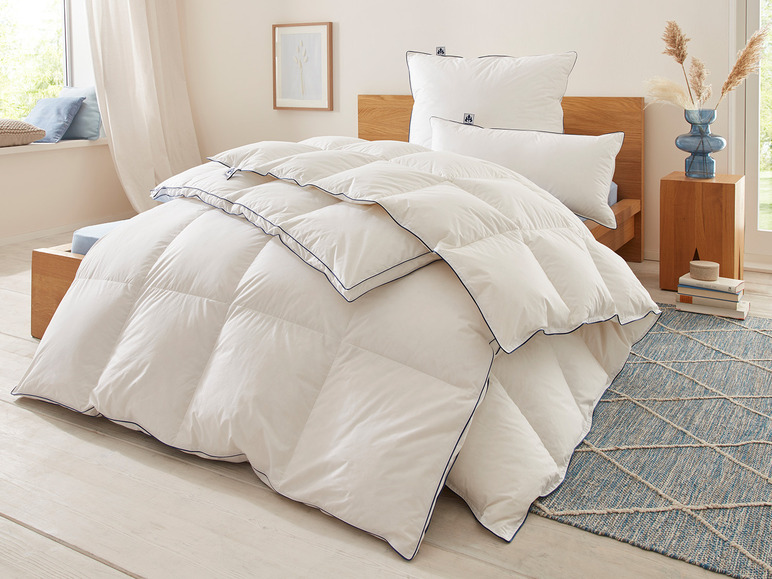 Eine weiße Daunendecke mit blauen Paspeln auf einem Bett mit Kissen.