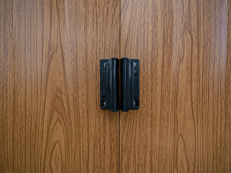 Zwei schwarze Griffe an einer Holztür.