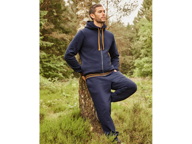 Mann in einem blauen Hoodie und Jogginghose im Wald.