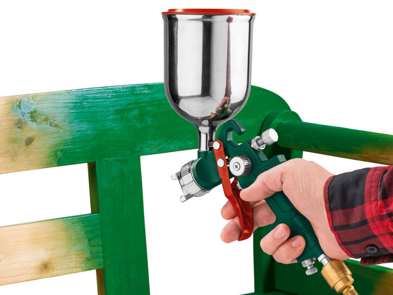 Eine Hand hält eine Spritzpistole und streicht damit eine Holzbank.
