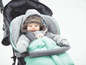 Ein Baby in einem grünen Winterschlafsack in einem schwarzen Kinderwagen.