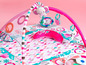 Babygym mit Spielmatte, Bogen und Hängespielzeug in rosa und grau.