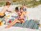 Eine Frau mit drei Kindern spielt am Strand mit einer gestreiften Strandmatte.