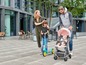 Eine Familie mit einem Baby im Kinderwagen, ein Kind auf einem Roller und die Eltern, die daneben gehen.