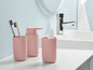 Rosa Badezimmerzubehör, darunter ein Seifenspender und zwei Becher.