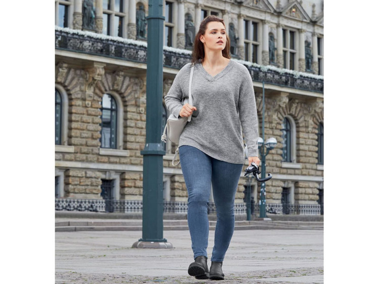 Eine Frau in einem grauen Pullover, blauen Jeans und schwarzen Stiefeln.